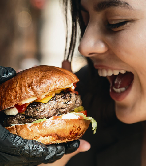 Person about to take a large bite of a gourmet burger with black gloves on.